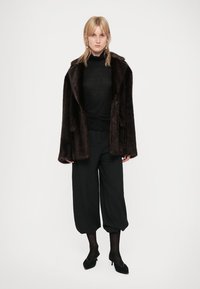 Brown faux fur coat with a relaxed fit, featuring a notched collar and two buttons, paired with black top and loose black trousers.