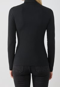 Svart långärmad polotröja, figurnära design, slät textur, hög krage och rak nederkant, bärs med mörka denimjeans.