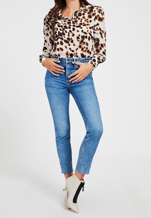 Kobieta ubrana w bluzkę z długim rękawem w panterkę, niebieskie jeansy z wysokim stanem i postrzępionymi brzegami oraz białe, szpiczaste botki z czarnymi suwakami.