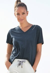 Dark navy V-neck t-shirt in soft fabric, featuring short sleeves and a logo detail on the shoulder. Worn with light-colored drawstring pants.