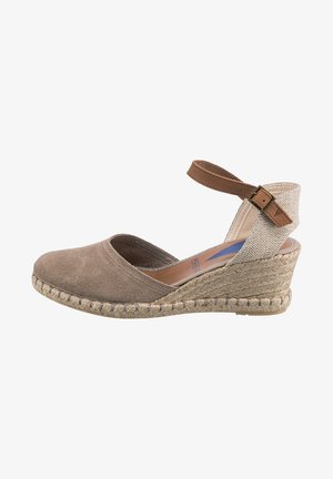 Cuñas de espadrille beige con parte superior texturizada, puntera de ante y suela de yute trenzado. Correa ajustable para el tobillo en tono marrón y diseño de talón abierto.