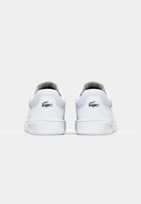 Baskets en cuir blanc avec une texture lisse, une forme arrondie, un design minimaliste et le logo noir de Lacoste sur le talon arrière.