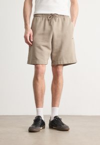 I pantaloni corti beige in felpa presentano una cintura elastica con cordoncino, tasche laterali e una vestibilità rilassata, realizzati in un tessuto morbido con una texture liscia.