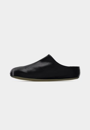 Zapato negro de cuero sin cordones con acabado liso, puntera redondeada y suela de goma baja y flexible. Diseño minimalista sin herrajes visibles.