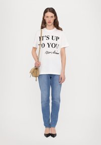 Vit t-shirt med svart text "DET ÄR UPP TILL DIG" och en signatur, tillsammans med ljusblå jeans och svarta spetsiga klackskor. Brun axelväska.