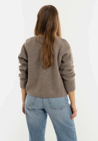 Grijze geribde trui met een ronde halslijn en lichtjes bolletjesmouwen, gecombineerd met lichtblauwe baggy jeans. De achterkant van de trui is zichtbaar.