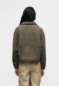 Κοντό μπουφάν από φλις σε ελιά με γιακά που διπλώνει προς τα κάτω και μανίκια σε αντίθετο χρώμα. Μαλακή υφή και άνετη εφαρμογή που συμπληρώνουν το στυλ με παντελόνια utility.