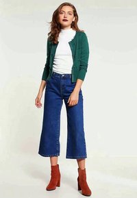Green cardigan, white turtleneck, blue wide-leg jeans, and brown ankle boots. Simple design with buttons on cardigan. Smooth textures.