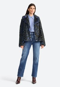 Veste en fausse fourrure à imprimé léopard noir et bleu, avec un large col et une fermeture à boutons. Associée à une chemise rayée et à un jean en denim.