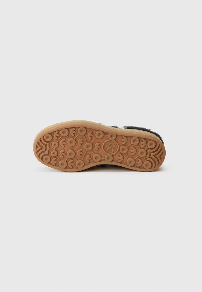 Gummisohlen-Sneaker mit einer strukturierten Gummiaußensohle, die über kreisförmige Grip-Muster verfügt, sowie einem weichen, dunklen Obermaterial mit einer flauschigen Textur.
