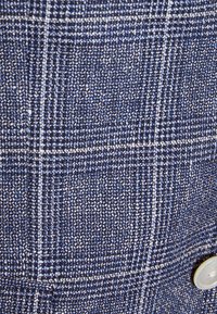 Marinblått texturerat tyg med ett rutig mönster, som innehåller vita och ljusblå trådar; inkluderar en vit knappdetalj.