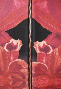 Tissu à motifs floraux dans des tons de rouge et de rose avec une fermeture éclair noire centrale. Texture lisse, présentant de grands motifs floraux et des formes abstraites.