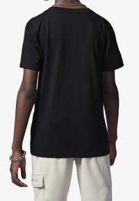 Czarny bawełniany t-shirt z krótkim rękawem, okrągłym dekoltem i gładką teksturą, noszony z kremowymi spodniami z detalem kieszeni.