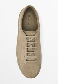 Beige suede sneaker with flat laces, rounded toe, embossed branding, and a gum sole. Smooth texture with minimalistic design.
