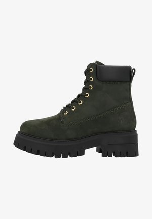 Bottine vert foncé à tige basse avec semelle épaisse crantée noire, col rembourré, fermeture à lacets avec œillets dorés et logo discret sur le talon.