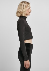 Sort cropped langærmet top med høj hals, lavet af et glat stof. Matchet med tætsiddende sorte fløjlsleggings.