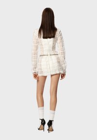 Weißes, strukturiertes Mini-Kleid mit durchsichtigen langen Ärmeln und tailliertem Oberteil. Es verfügt über einen verdeckten Reißverschluss auf der Rückseite und einen dezenten Taillenakzent.