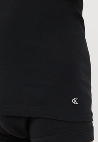 Juodas dryžuotas marškinėlis be rankovių su mažu baltu "cK" logotipu apatinėje dalyje, pagamintas iš lygaus medvilnės mišinio.