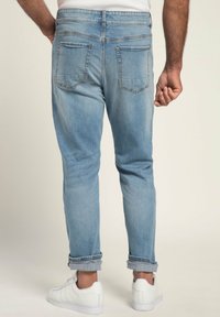 Jeans de mezclilla azul claro con un corte relajado, puños enrollados y dos bolsillos traseros. Combinados con zapatillas blancas.