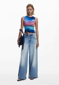 Viacfarebné tielkové tričko s priliehavým strihom v kombinácii s širokými svetlomodrými džínsami s vyblednutou textúrou a vysokým pásom.