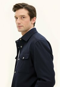 Giacca camicia blu navy realizzata in un tessuto resistente, con colletto a punta, bottoni a scatto e tasca sul petto.