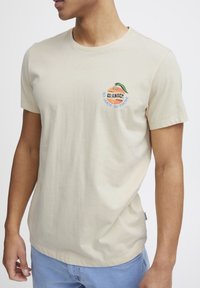 Beige bomulds t-shirt med et farverigt broderet orange design på brystet med teksten "So Juicy So Fresh." Korte ærmer og rund hals.