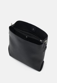 Sac fourre-tout en cuir noir à texture lisse, doté d'un grand compartiment principal, d'une poche zippée et d'une fermeture à bouton-pression.