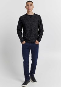 Schwarzer melierterPullover mit langen Ärmeln, Rundhalsausschnitt und gerippten Bündchen, kombiniert mit dunkelblauen Slim-Fit-Jeans und schwarzen Turnschuhen.