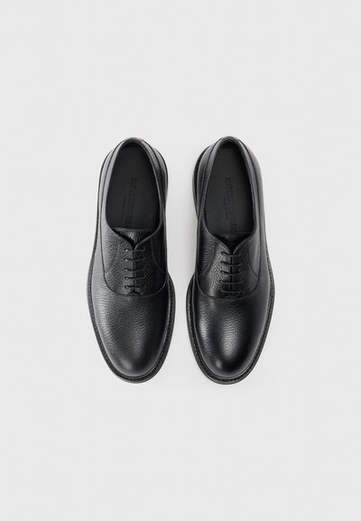Black leather shoes featuring a textured finish, rounded toe, lace-up design, and smooth accents along the edges.