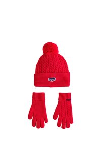 Rød strikket hue med pompon og ribkant, ledsaget af matchende ribstrikkede handsker med kabelstrikkede detaljer.