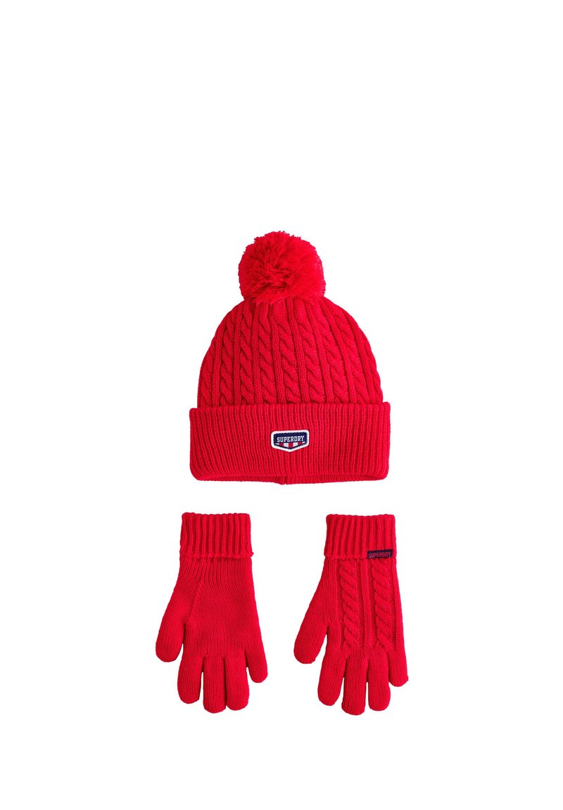 Rød strikket hue med pompon og ribkant, ledsaget af matchende ribstrikkede handsker med kabelstrikkede detaljer.