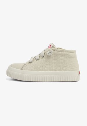 Zapatilla alta de lona de color claro con cordones grises, suela de goma y una pequeña etiqueta de logo roja en el lateral. Superficie texturizada con punta redondeada.