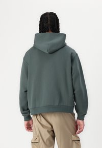 Zelena kapuca s sproščenim krojem. Ima kenguru žep, rebraste manšete in dno. Narejena iz mehkega teksturiranega blaga.