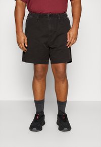 Sorte bomuldsnyder med elastisk talje, sidelommer og knælang længde, parret med grå sokker og sorte sneakers.
