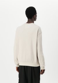 Lys beige teksturert sweatshirt med ribbet stoff, rund halslinning og mansjetter. Har subtil hvit broderi på baksiden.
