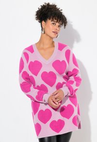 Overversie V-hals trui in lichtroze met grote fuchsia hartpatronen. Zachte textuur, geribbelde afwerking bij de mouwen en onderkant, ontspannen pasvorm.