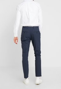Marineblauwe dress pants gemaakt van een getextureerde stof met een slim fit, met achterzakken en een tailleband. Gecombineerd met een wit shirt en sneakers.