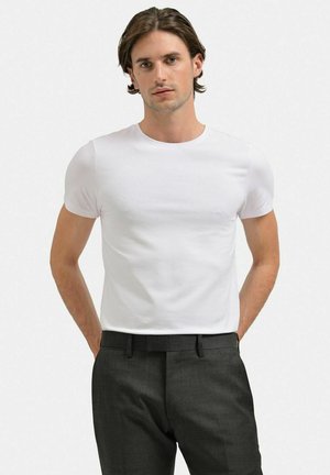 Vit t-shirt med rund hals i bomull, med korta ärmar och en åtsittande design, kombinerad med grå skräddarsydda byxor.