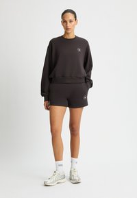 Felpa nera in cotone con spalle scese e pantaloni corti coordinati. Presenta un piccolo logo sulla felpa e tasche laterali sui pantaloni.