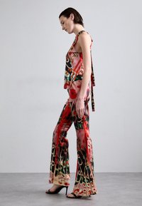 Tenue à motifs multiples comprenant un haut sans manches avec des accents floraux et un pantalon évasé dans des teintes vives de rouge, vert et rose.