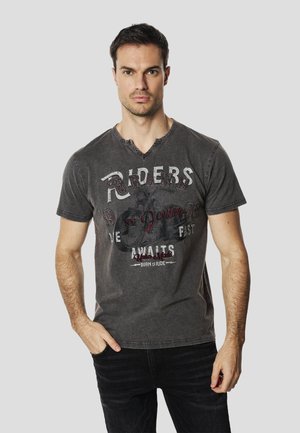 Camiseta de algodón gris con cuello en V y bordes desgastados que presenta una impresión gráfica, incluyendo la palabra "Riders" en letras negritas.