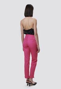 Zwarte rugloze top met beaded schouderbanden, gecombineerd met aansluitende roze trousers en zwarte hoge hakken, die een slanke silhuet benadrukken.