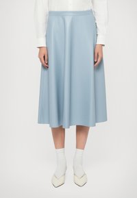 Gonna midi azzurro chiaro realizzata in tessuto morbido, con vita aderente e silhouette fluida, abbinata a calzini bianchi e scarpe a punta.