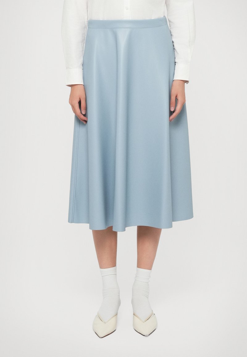 Gonna midi azzurro chiaro realizzata in tessuto morbido, con vita aderente e silhouette fluida, abbinata a calzini bianchi e scarpe a punta.