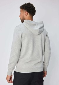 Sweat-shirt gris à capuche, ourlet et poignets côtelés. Tissu doux, manches longues et coupe décontractée. Vue arrière montrant la capuche et les coutures.