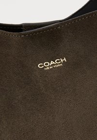 Brown suede ankle boot with a rounded toe, featuring a gold "COACH NEW YORK" logo near the opening and smooth stitching detail.