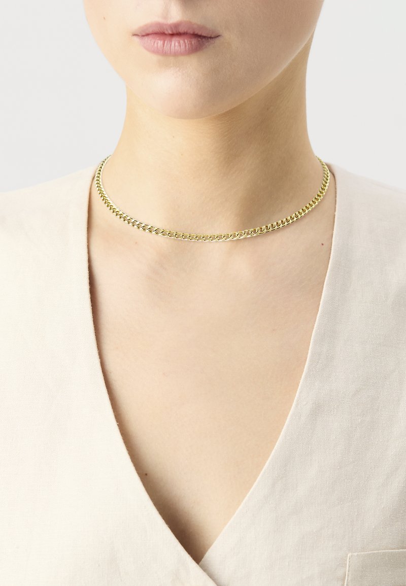 Zlatá reťazová choker náhrdelník s plochým dizajnom, obsahujúca prepojené články; vystavená na neutrálnom odeve.