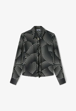 Camisa negra con un patrón geométrico de puntos y corazones blancos, de manga larga, con cuello y cierre de lazo en el frente. Textura de tela suave.