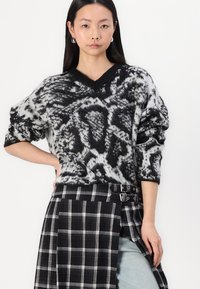 Maglione lavorato a maglia bianco e nero con scollo a V e maniche oversize, caratterizzato da una stampa animale testurizzata, abbinato a una gonna a quadri.