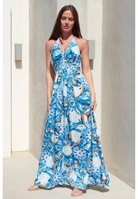 Halterneck maxi kjole i blå, med blomster mønstre i forskellige nuancer, samlet bodice og flydende fuld nederdel. Glat stof tekstur.